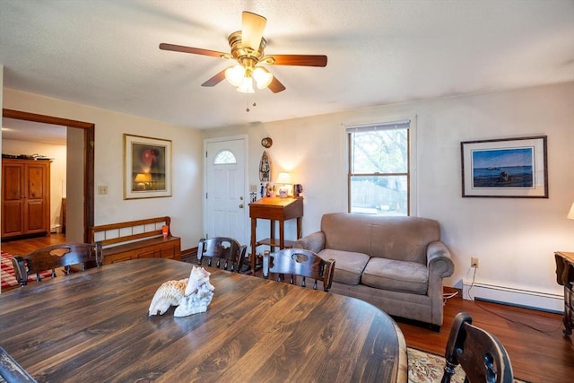 living area featuring a ceiling fan, a baseboard heating unit, wood finished floors, and baseboards