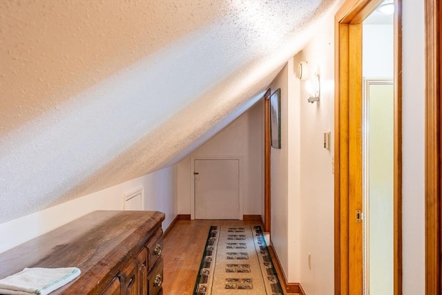 bonus room with a textured ceiling, vaulted ceiling, and light wood finished floors