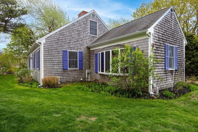 view of side of home with a chimney, a yard, and a shingled roof