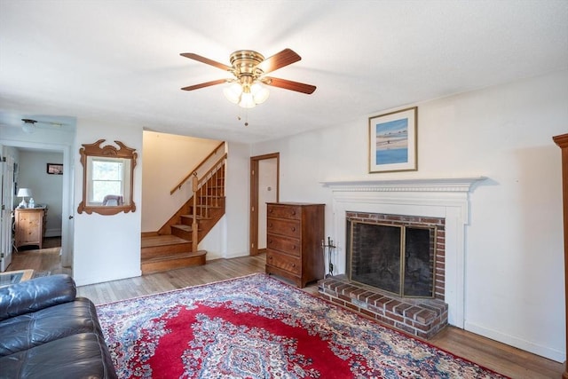 living room featuring a ceiling fan, wood finished floors, a fireplace, and stairway