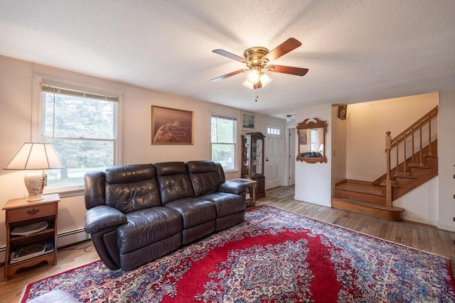 living area with ceiling fan, wood finished floors, stairs, a textured ceiling, and baseboard heating