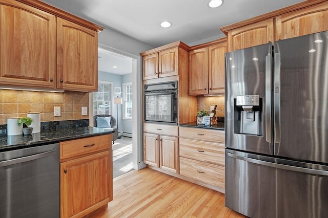 kitchen featuring light wood-style flooring, dark stone countertops, recessed lighting, appliances with stainless steel finishes, and decorative backsplash