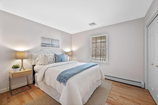 bedroom featuring a baseboard heating unit, visible vents, wood finished floors, and a closet