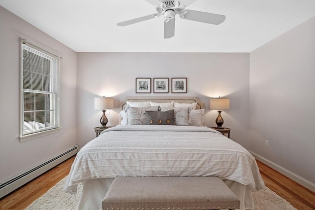 bedroom with a baseboard heating unit, wood finished floors, baseboards, and a ceiling fan