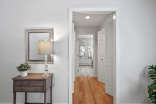 corridor with a baseboard radiator, baseboards, and light wood-style flooring