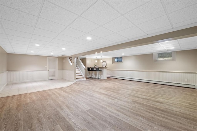 below grade area featuring wood finished floors, stairs, a wall mounted air conditioner, wainscoting, and baseboard heating