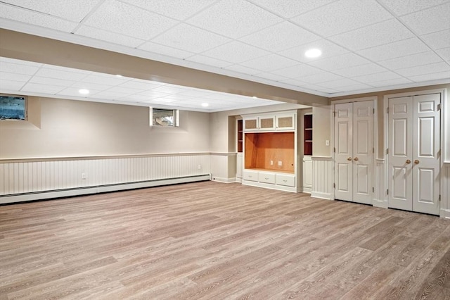 below grade area with a baseboard heating unit, wood finished floors, and a drop ceiling