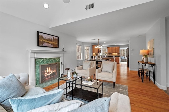 living area with light wood finished floors, visible vents, baseboards, a chandelier, and a fireplace