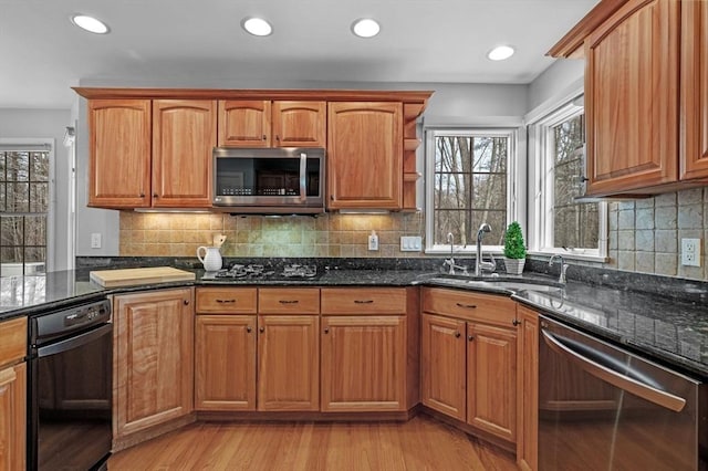 kitchen featuring a sink, dark stone counters, light wood-style flooring, and stainless steel appliances