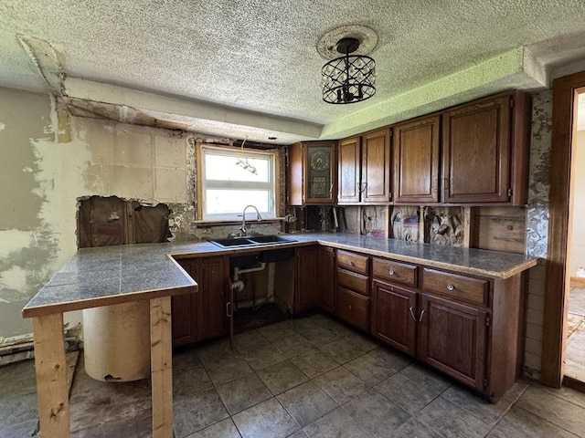 kitchen featuring a sink, a textured ceiling, a peninsula, tile counters, and dark tile patterned flooring