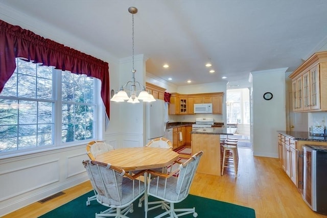 dining room featuring light wood-type flooring, visible vents, ornamental molding, a decorative wall, and a chandelier