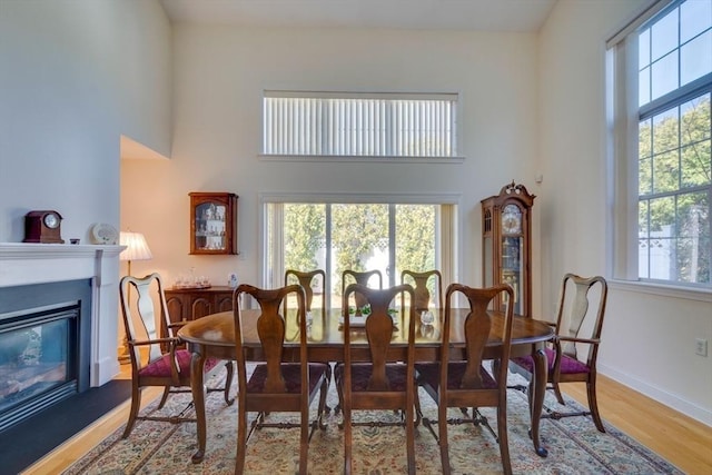 dining area with plenty of natural light, a towering ceiling, a glass covered fireplace, and wood finished floors