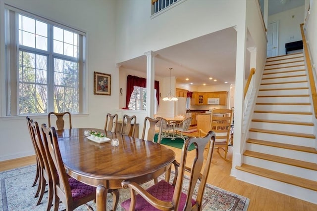 dining area with light wood finished floors, baseboards, stairs, an inviting chandelier, and a towering ceiling