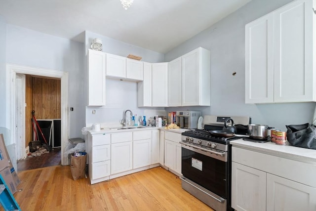 kitchen featuring light countertops, light wood-style flooring, white cabinets, stainless steel range with gas stovetop, and a sink