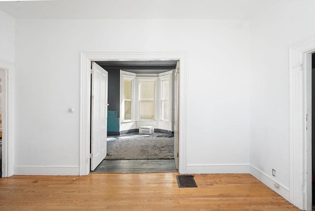 hall with light wood finished floors, visible vents, and baseboards