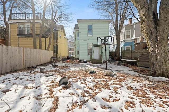 snow covered rear of property featuring entry steps and fence