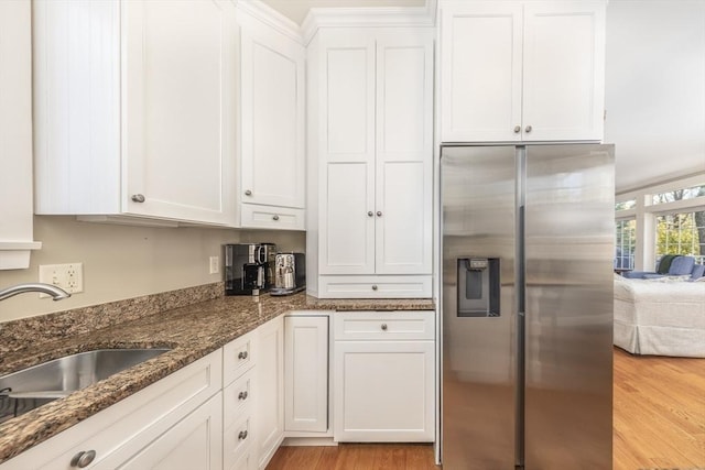 kitchen with dark stone countertops, stainless steel fridge with ice dispenser, white cabinets, and light hardwood / wood-style floors