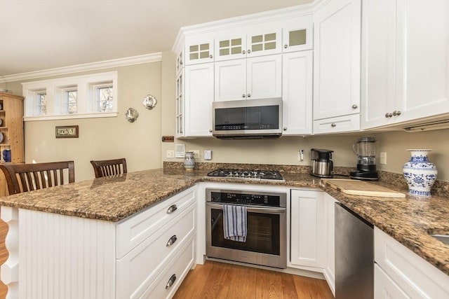 kitchen featuring white cabinetry, stainless steel appliances, dark stone countertops, crown molding, and light hardwood / wood-style floors