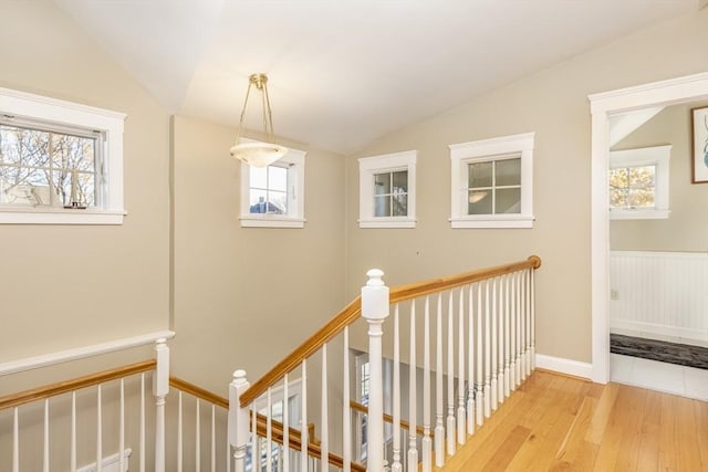 corridor with light wood-type flooring, vaulted ceiling, and a wealth of natural light