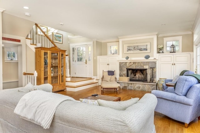 living room featuring a healthy amount of sunlight, a stone fireplace, ornamental molding, and light hardwood / wood-style flooring