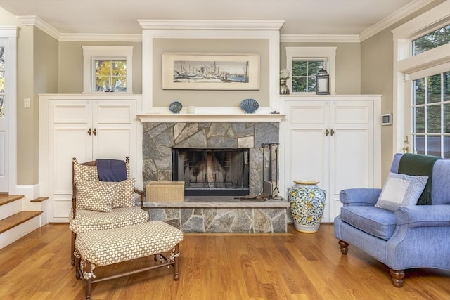 sitting room with a stone fireplace, crown molding, and light hardwood / wood-style flooring