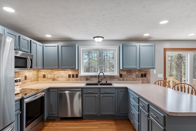 kitchen featuring recessed lighting, a sink, light wood-style flooring, a peninsula, and appliances with stainless steel finishes
