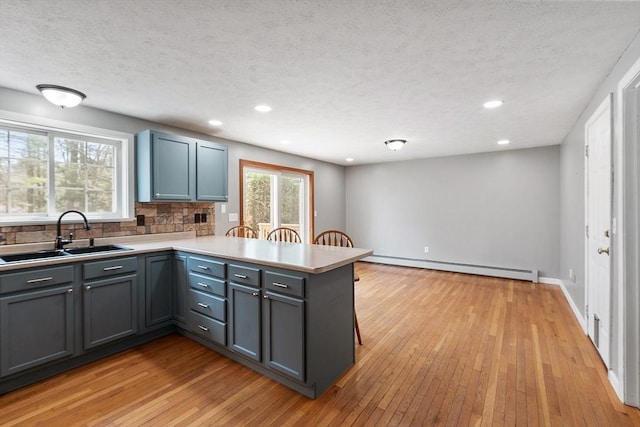 kitchen featuring a baseboard heating unit, backsplash, a sink, light wood-type flooring, and a peninsula
