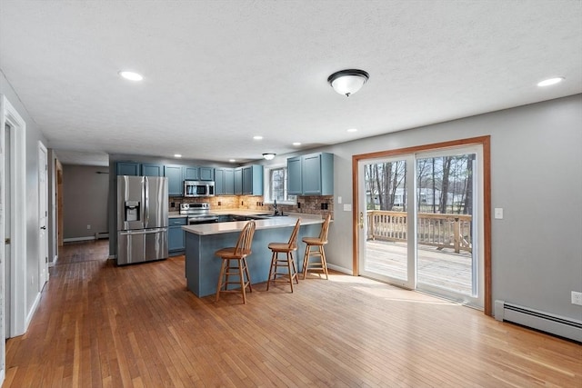 kitchen with blue cabinets, a baseboard heating unit, appliances with stainless steel finishes, a sink, and a peninsula