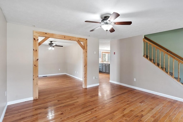 unfurnished room featuring stairway, a ceiling fan, light wood finished floors, and baseboards