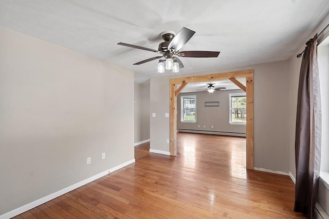 spare room featuring baseboard heating, baseboards, ceiling fan, and light wood-style floors