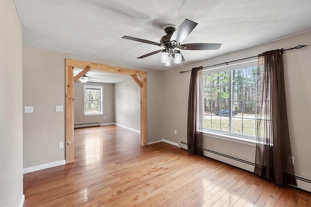 unfurnished room with baseboard heating, ceiling fan, a healthy amount of sunlight, and light wood finished floors