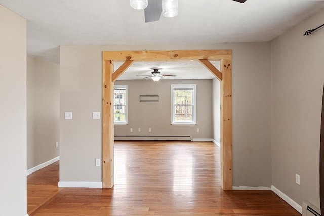 unfurnished room featuring a baseboard heating unit, a ceiling fan, wood finished floors, and baseboards