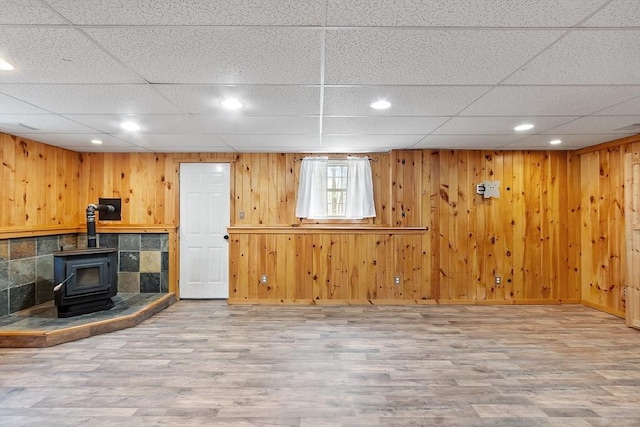unfurnished living room with a wood stove, recessed lighting, a drop ceiling, and wood finished floors