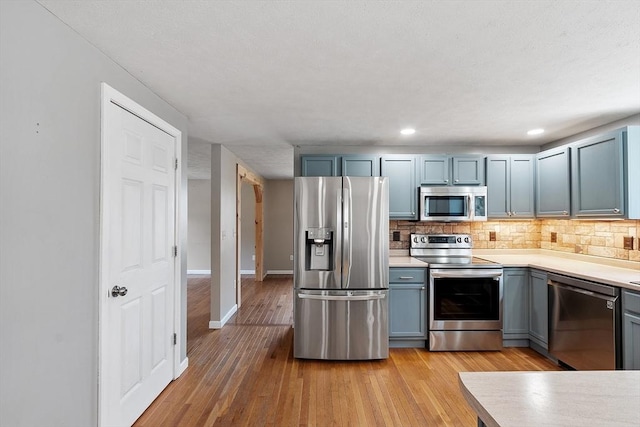 kitchen featuring appliances with stainless steel finishes, decorative backsplash, light wood finished floors, and light countertops