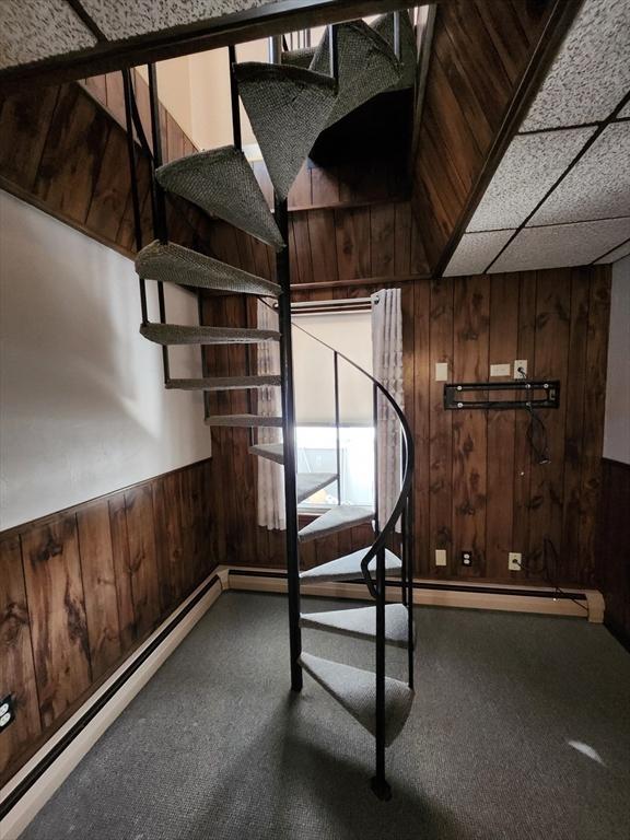 stairs with baseboard heating, a paneled ceiling, and wooden walls