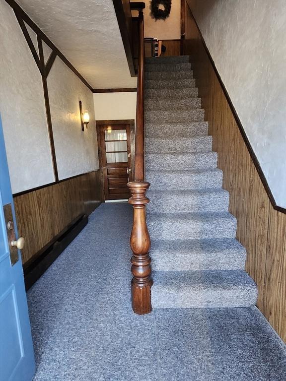 stairway with a textured ceiling, carpet floors, ornamental molding, and wood walls