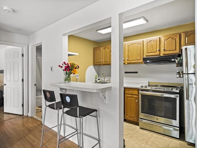 382 Great Rd Unit B103, Acton, MA 01720 - kitchen with under cabinet range hood, appliances with stainless steel finishes, a breakfast bar area, a sink, and light countertops
