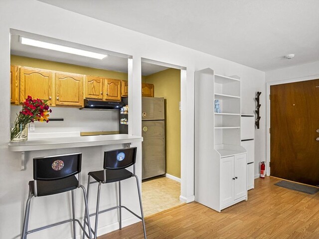 382 Great Rd Unit B103, Acton, MA 01720 - kitchen with range hood, a breakfast bar area, freestanding refrigerator, light wood-style flooring, and light countertops