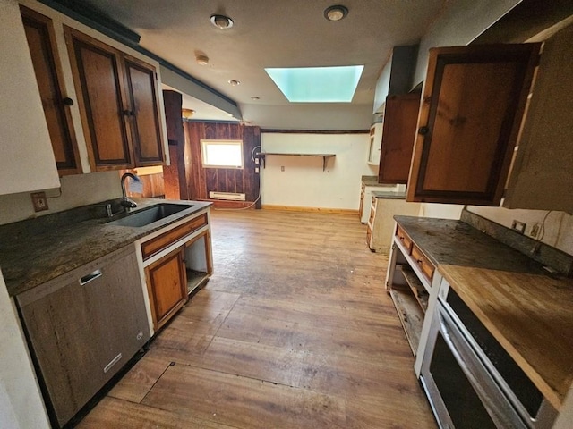 kitchen featuring a skylight, baseboards, a sink, and wood finished floors