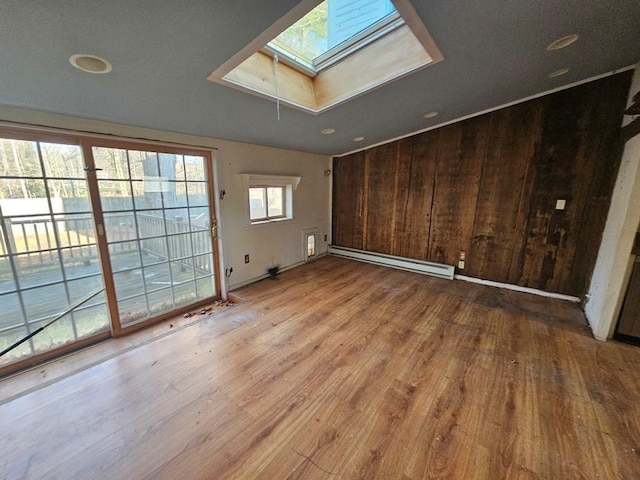 unfurnished room featuring a baseboard heating unit, a skylight, wood walls, and wood finished floors