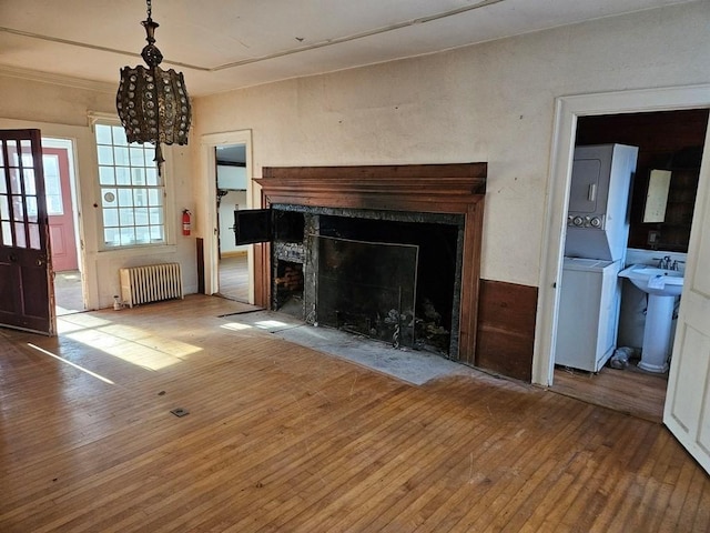 unfurnished living room featuring radiator heating unit, a premium fireplace, hardwood / wood-style floors, and stacked washer and clothes dryer