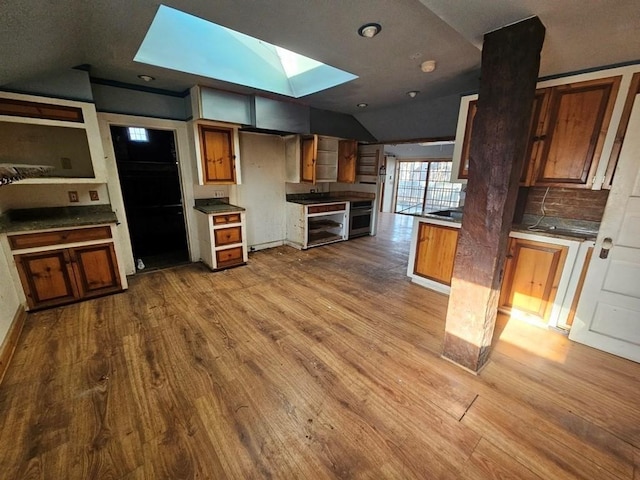 kitchen with lofted ceiling with skylight, wood finished floors, oven, and brown cabinets