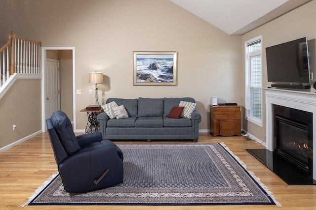 living room with baseboards, lofted ceiling, a glass covered fireplace, and light wood-type flooring