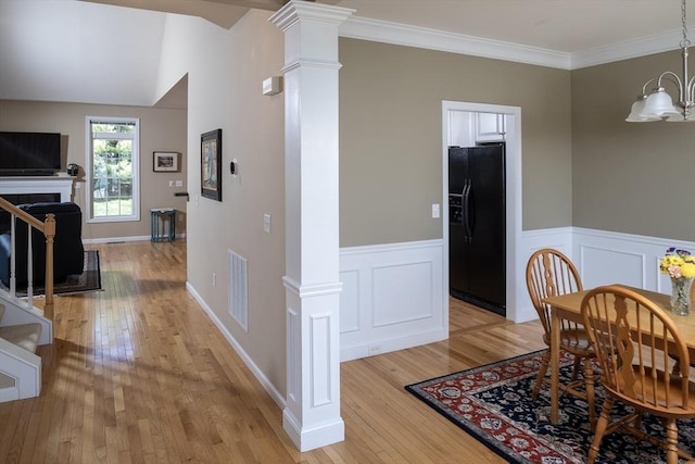 dining area featuring a wainscoted wall, light wood-style floors, visible vents, and ornate columns