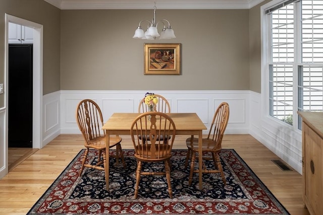 dining area featuring a chandelier, a wainscoted wall, light wood finished floors, ornamental molding, and visible vents