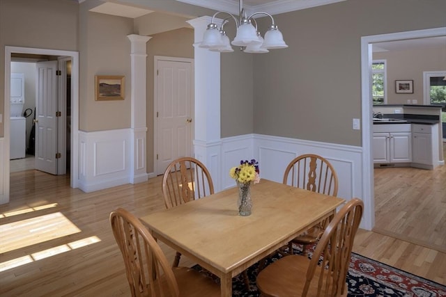 dining room featuring a decorative wall, wainscoting, light wood-style floors, stacked washer / drying machine, and a notable chandelier