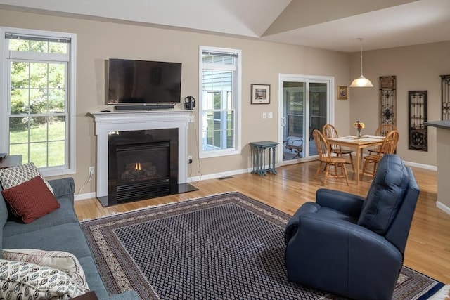 living area with a warm lit fireplace, wood finished floors, and a wealth of natural light