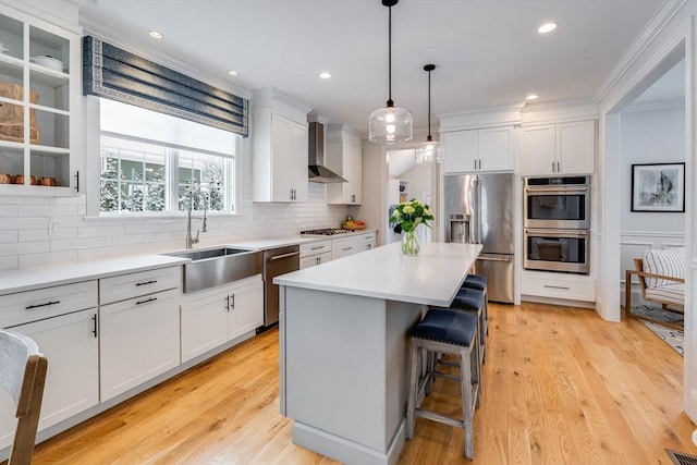 kitchen featuring appliances with stainless steel finishes, sink, wall chimney range hood, and white cabinets