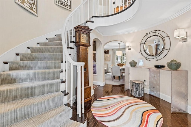 foyer entrance featuring arched walkways, ornamental molding, wood finished floors, and stairs