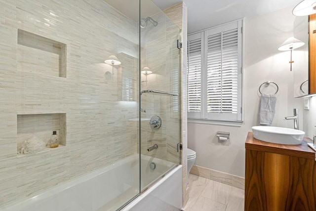 bathroom featuring toilet, combined bath / shower with glass door, vanity, and baseboards